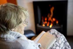 elderly woman reading book by a fire