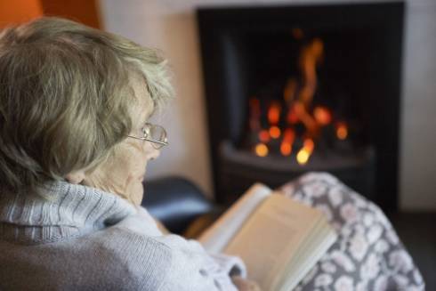 elderly woman reading a book by a fire