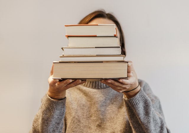 person holding stack of books in front of face