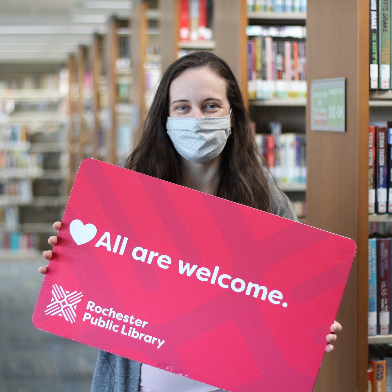 person holding magenta sign reading All Are Welcome